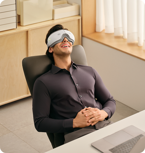 Mężczyzna relaksuje się w fotelu biurowym, używając masażera oczu SKG ES300, z laptopem na biurku