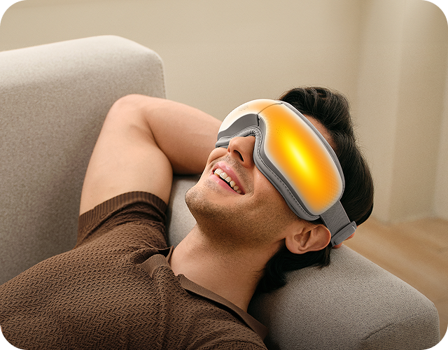 Mężczyzna relaksuje się na kanapie, używając masażera oczu SKG ES300 z aktywną funkcją gorącego kompresu