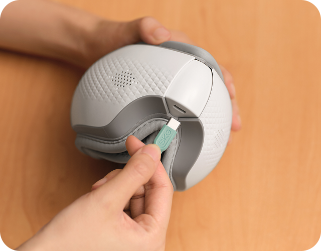 Ładowanie złożonego masażera oczu SKG ES300 za pomocą zielonej wtyczki USB (Universal Serial Bus) typu C