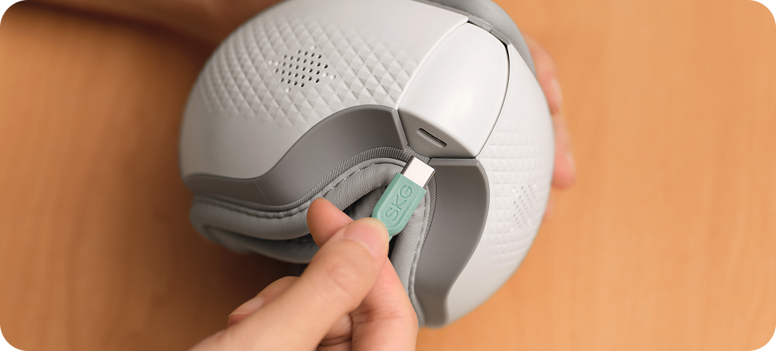 Ładowanie złożonego masażera oczu SKG ES300 za pomocą zielonej wtyczki USB (Universal Serial Bus) typu C