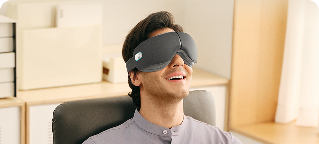 Mężczyzna siedzący w fotelu biurowym, używając szarego masażera oczu SKG ES500 podczas przerwy w pracy