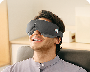 Mężczyzna siedzący w fotelu biurowym, używając szarego masażera oczu SKG ES500 podczas przerwy w pracy