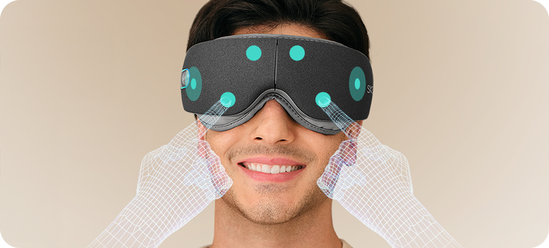 Mężczyzna uśmiecha się, używając szarego masażera oczu SKG ES500, z wizualizacją punktów masujących na twarzy