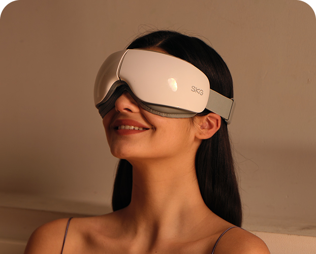 Kobieta siedząca w łóżku używa białego masażera oczu SKG ES500