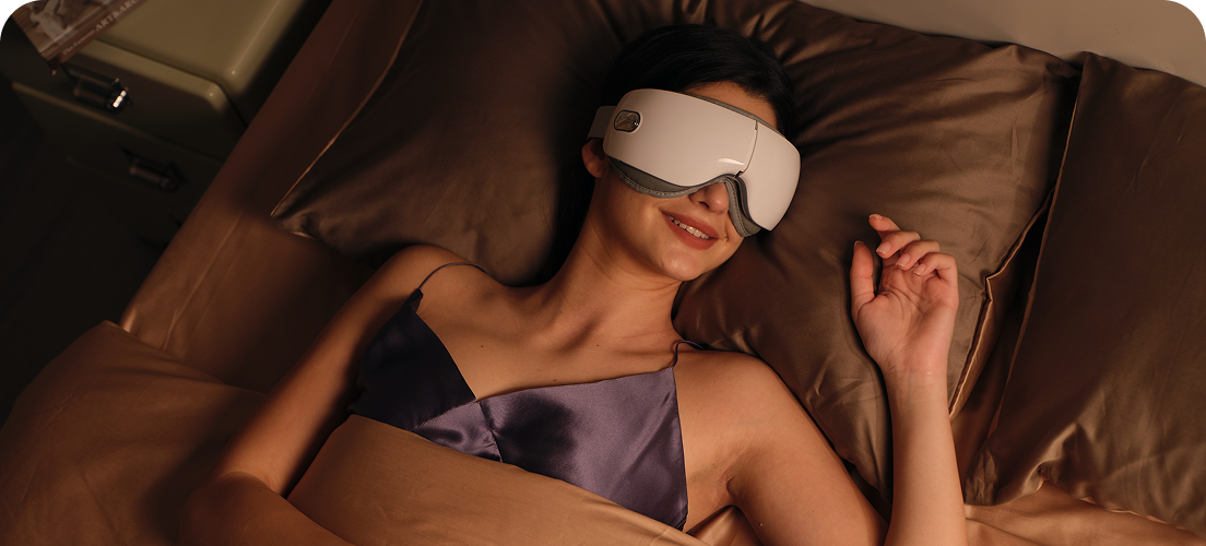 Kobieta leżąca w łóżku używa masażera oczu SKG ES500 w kolorze białym, podczas relaksu