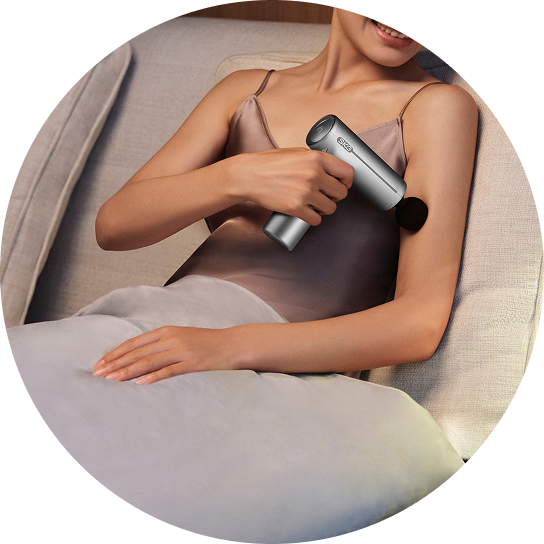 Kobieta leżąca w łóżku masuje ramię za pomocą pistoletu do masażu SKG F1-Pro w kolorze srebrnym