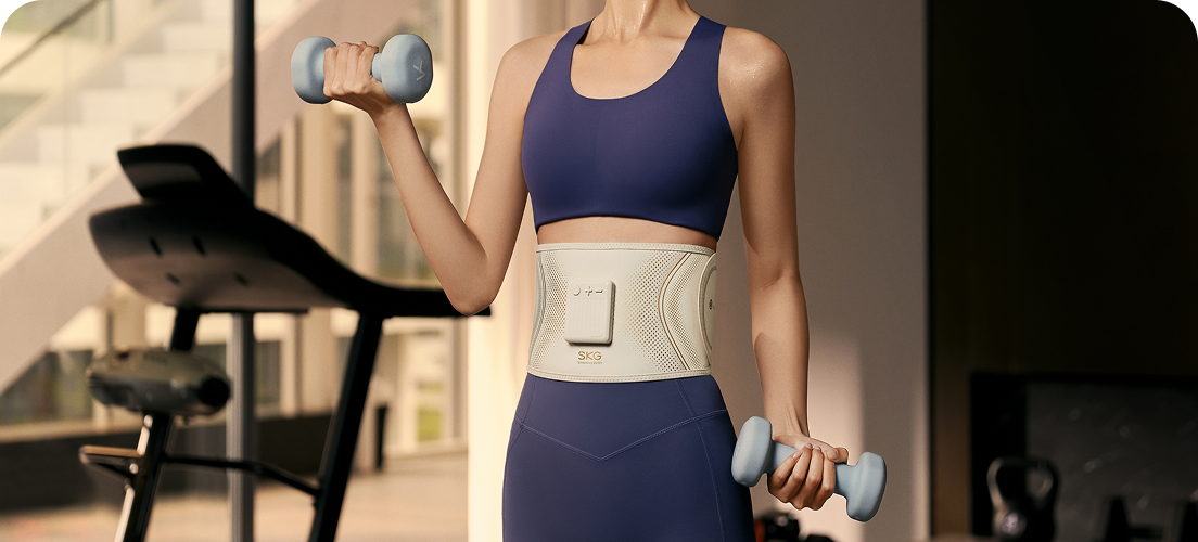 Kobieta ćwiczy z hantlami, mając na sobie pas treningowy SKG GS300 w kolorze beżowym, w nowoczesnej siłowni