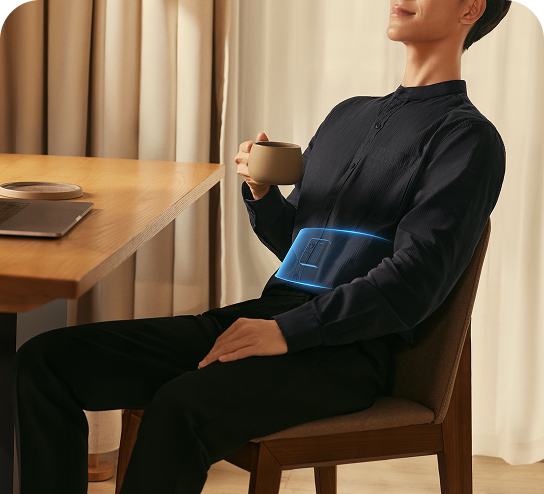 Mężczyzna siedzi przy biurku, pijąc kawę i używając pasa treningowego SKG GS300 z wizualizacją działania