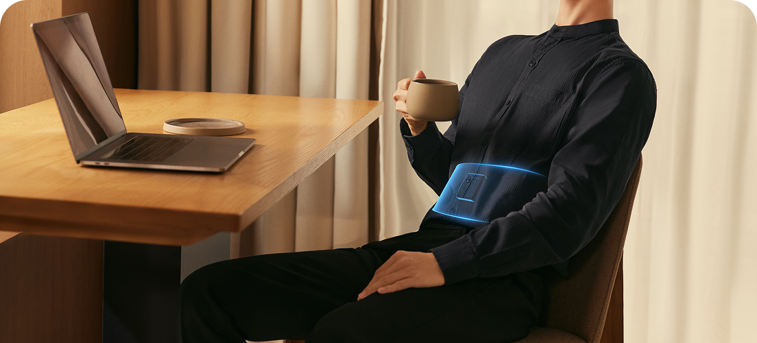 Mężczyzna siedzi przy biurku, pijąc kawę i używając pasa treningowego SKG GS300 z wizualizacją działania