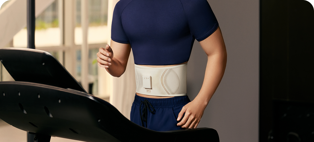 Mężczyzna biegnie na bieżni, używając pasa treningowego SKG GS300 w kolorze beżowym podczas ćwiczeń w domu