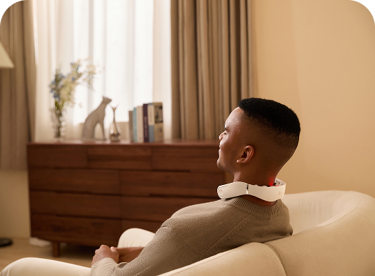 Mężczyzna relaksuje się w fotelu, używając masażera szyi SKG GS500-N ze świecącą czerwoną diodą na karku