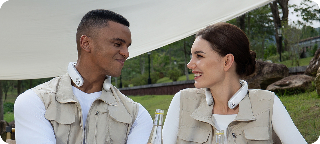 Para siedzi przy drewnianym stole kempingowym, używając białych masażerów szyi SKG GS500-N