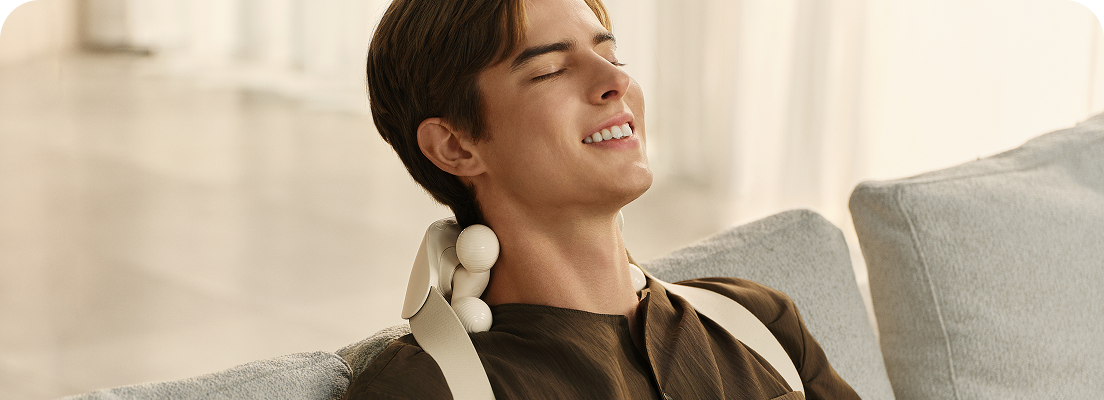 Mężczyzna siedzący na kanapie z zamkniętymi oczami używa masażera karku SKG HS500-2 w kolorze beżowym