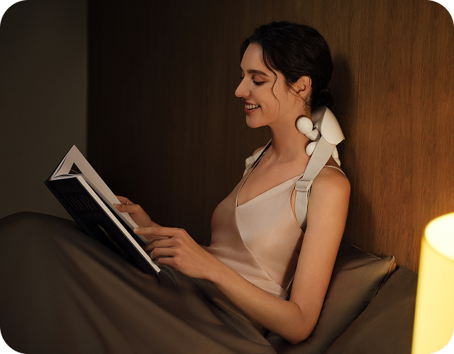 Kobieta w łóżku czyta książkę, używając masażera karku SKG HS500-2 z dwoma ruchomymi głowicami masującymi