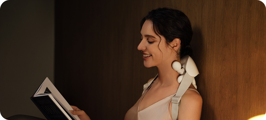 Kobieta w łóżku czyta książkę, używając masażera karku SKG HS500-2 z dwoma ruchomymi głowicami masującymi