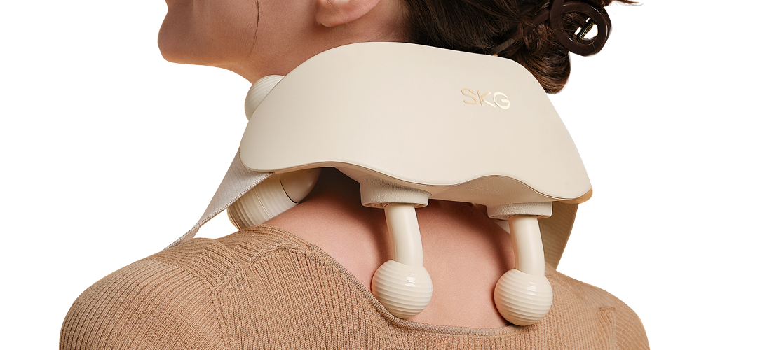 Masażer karku SKG HS500-2 w kolorze beżowym, z dwoma kulistymi głowicami, na karku uśmiechniętej kobiety