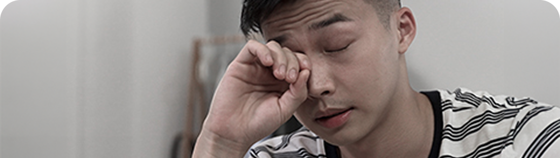 Mężczyzna w koszulce w paski, z zamkniętymi oczami, pociera dłonią powiekę, wyrażając zmęczenie