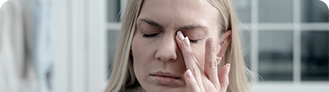 Kobieta z zamkniętymi oczami i zmartwioną miną dotyka palcami skroni, prawdopodobnie odczuwając ból lub zmęczenie.