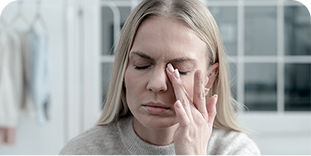 Kobieta z zamkniętymi oczami i zmartwioną miną dotyka palcami skroni, prawdopodobnie odczuwając ból lub zmęczenie.