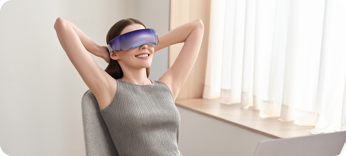 Uśmiechnięta kobieta w biurze relaksuje się w fotelu, używając futurystycznego masażera oczu SKG KS700