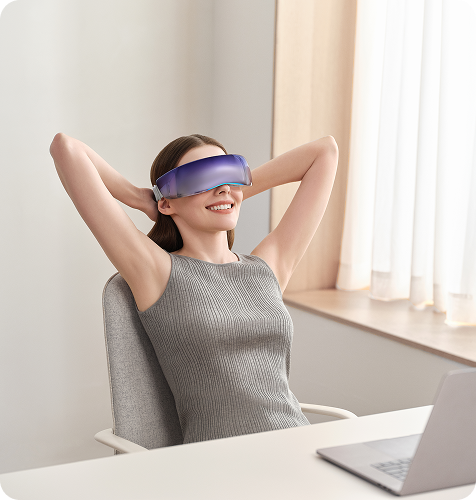 Uśmiechnięta kobieta w biurze relaksuje się w fotelu, używając futurystycznego masażera oczu SKG KS700