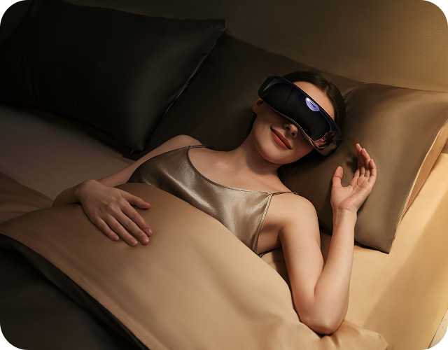 Kobieta relaksuje się w łóżku z masażerem oczu SKG KS700 na twarzy, w ciepłym, przyciemnionym świetle.