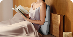 Kobieta czyta książkę w łóżku, opierając plecy o masażer SKG TS700 z widocznym czerwonym światłem
