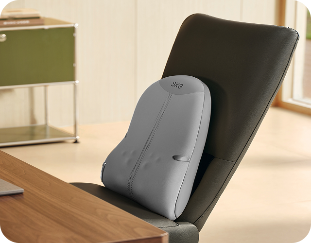Szary masażer pleców SKG TS700 zamocowany na fotelu biurowym obok laptopa na nowoczesnym drewnianym biurku