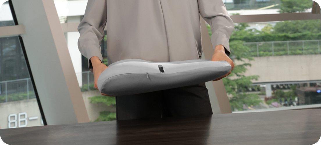 Kobieta w biurze pochyla się nad stołem, trzymając w rękach szary masażer pleców SKG TS700