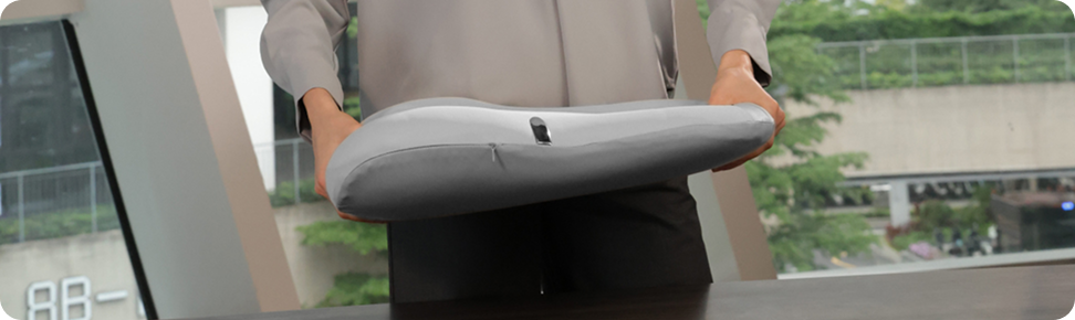 Kobieta w biurze pochyla się nad stołem, trzymając w rękach szary masażer pleców SKG TS700