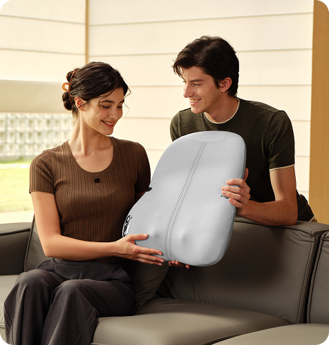 Uśmiechnięta para na kanapie, mężczyzna podaje kobiecie szary masażer pleców SKG TS700