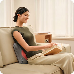 Uśmiechnięta kobieta czyta książkę, siedząc na kanapie i używając masażera pleców SKG VS500 z podgrzewaniem