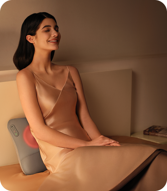 Kobieta w jedwabnej sukience relaksuje się w łóżku, używając masażera pleców SKG VS500 z funkcją podgrzewania
