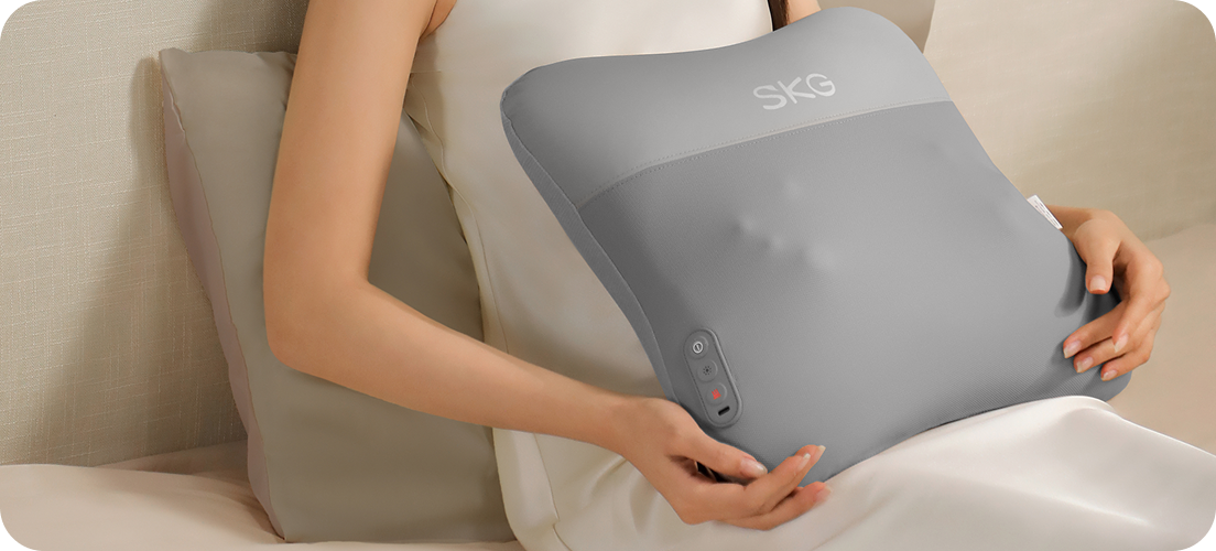 Kobieta relaksuje się na kanapie, używając masażera pleców SKG VS500 w kształcie poduszki na swoim brzuchu