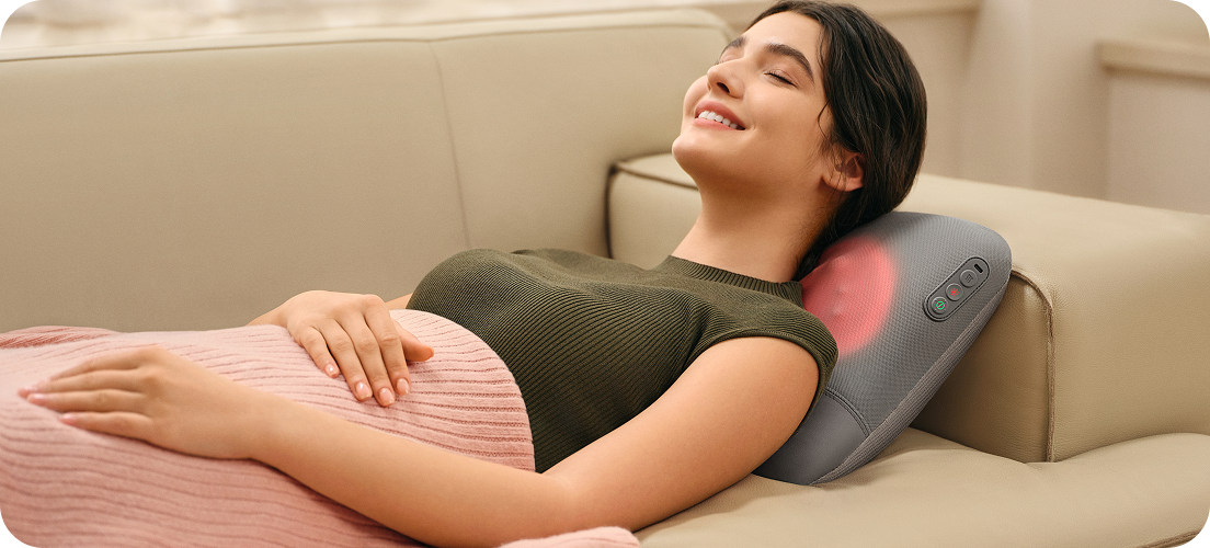 Uśmiechnięta kobieta leży na kanapie, używając masażera pleców SKG VS500 z funkcją podgrzewania szyi