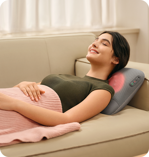 Uśmiechnięta kobieta leży na kanapie, używając masażera pleców SKG VS500 z funkcją podgrzewania szyi