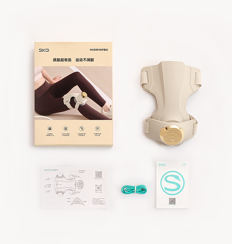 Widok z góry na zestaw masażera kolan SKG WS500: urządzenie, instrukcja, ulotka z logo 'S' i kabel