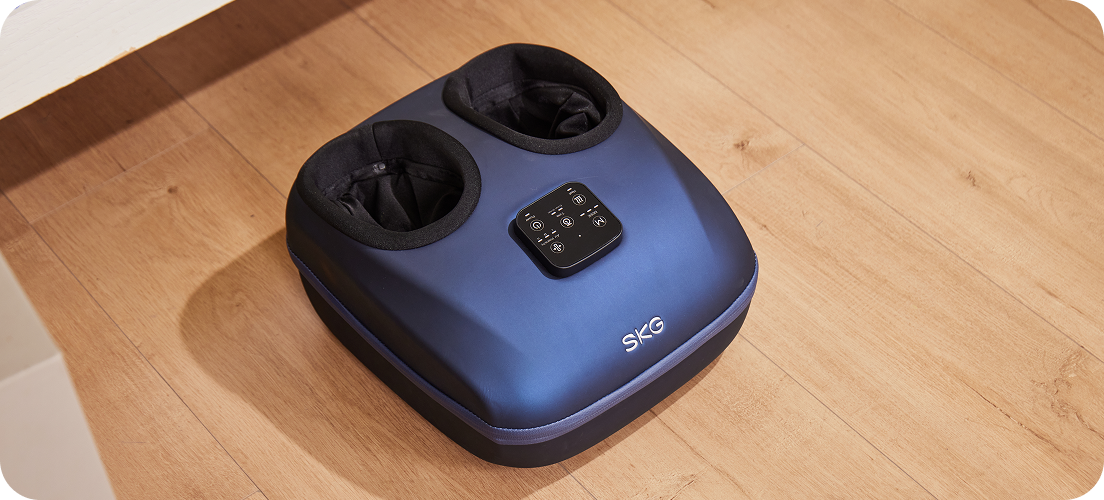 Masażer stóp SKG YS100 w kolorze granatowym, z pilotem na obudowie, leżący na drewnianej podłodze w domu