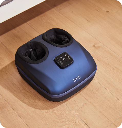 Masażer stóp SKG YS100 w kolorze granatowym, z pilotem na obudowie, leżący na drewnianej podłodze w domu